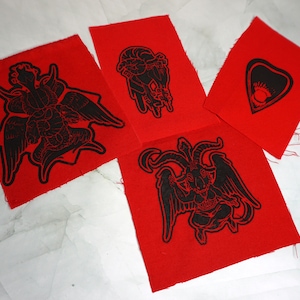 May include: Four red fabric patches with black iron-on designs. The designs include a winged serpent, a heart with a star inside, a winged goat with horns, and a hand with a heart and a chain.