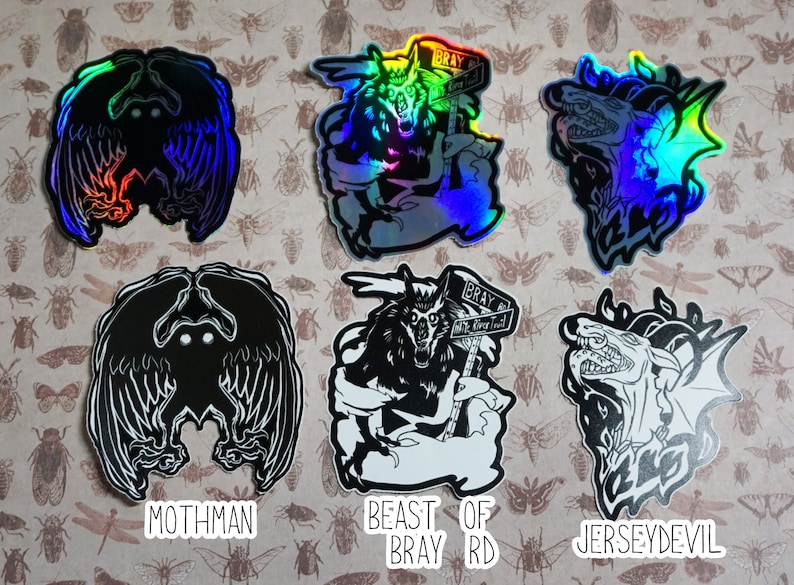 May include: Six holographic stickers featuring black and white illustrations of mythical creatures. The stickers are on a background of brown paper with a pattern of insects. The stickers are labeled "Mothman", "Beast of Bray Rd", and "Jersey Devil".