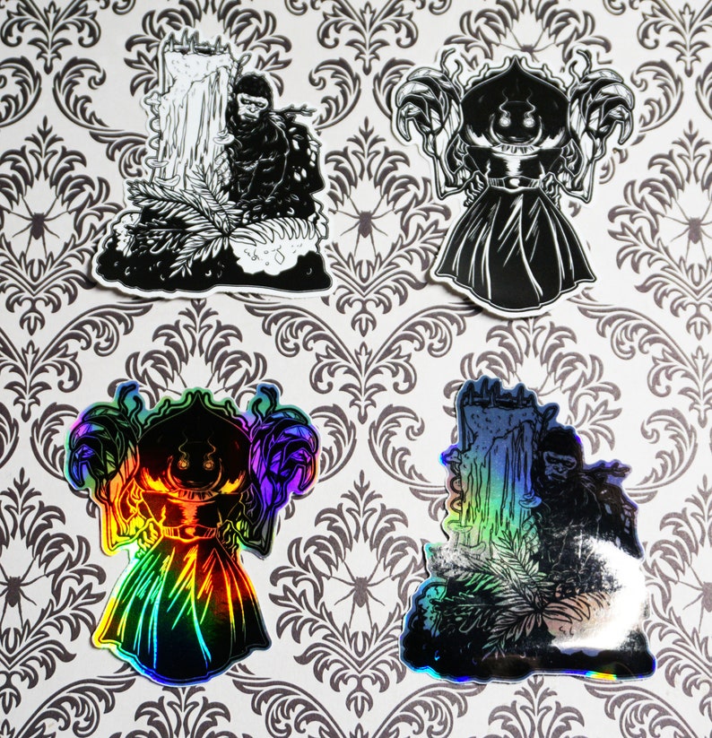 May include: Four black and white stickers with a spooky theme. The stickers feature a ghost, a monster, and two figures standing in front of a waterfall. The stickers are printed on a white background.