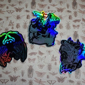 May include: Three iridescent holographic stickers featuring mythical creatures. The first sticker shows a wolf with a crown and the text "BRAY". The second sticker shows a bird with wings spread. The third sticker shows a dragon with its mouth open.