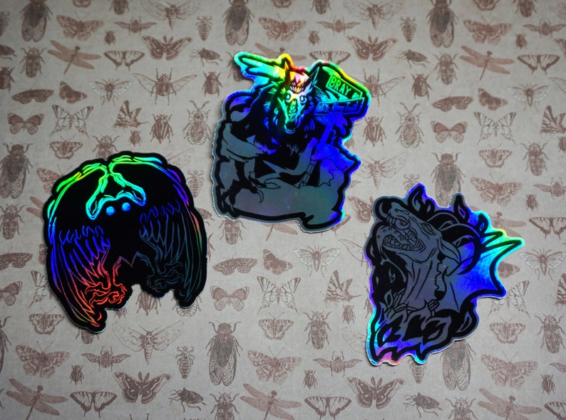 May include: Three iridescent holographic stickers featuring mythical creatures. The first sticker shows a wolf with a crown and the text "BRAY". The second sticker shows a bird with wings spread. The third sticker shows a dragon with its mouth open.