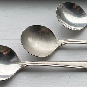 Puede incluir: Tres cucharas de plata con mangos ornamentados. Las cucharas tienen una forma de cuenco redondeada y están dispuestas en fila.