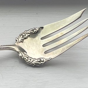 May include: A silver fork with a beaded handle and ornate design on the tines and back of the head.