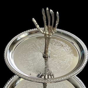 May include: Two-tiered silver serving tray with an ornate design and a skeletal hand as the centre post.