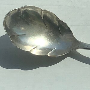 May include: A silver sugar spoon with a decorative, leaf-shaped bowl.