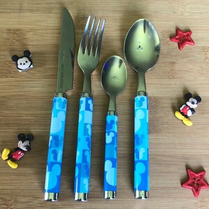 May include: A set of four blue and white Mickey Mouse themed silverware, including a knife, fork, and two spoons. The handles feature a repeating pattern of Mickey Mouse heads.