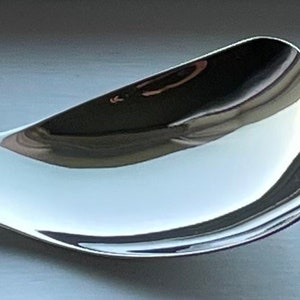 May include: A silver spoon with a unique curved handle and a wide, shallow bowl.