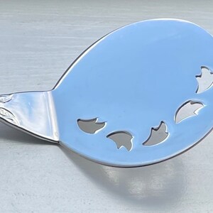 May include: A silver serving spoon with a decorative handle and a round, openwork bowl with cut-out leaf shapes.