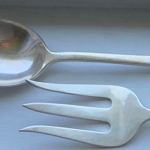 May include: A silver serving set with a spoon and fork. The spoon has a rounded bowl and a long handle. The fork has three tines and a long handle.