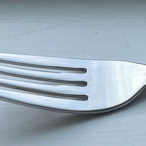 May include: A silver fork with a gold-trimmed handle. The handle has a decorative design.