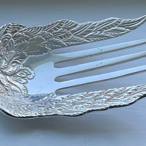 May include: A silver serving fork with an ornate, floral design. The fork has three tines and a long handle.