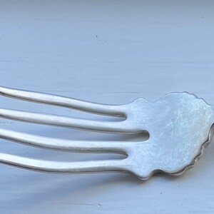 Peut inclure: Une fourchette en argent avec un manche orné d'un motif floral. La fourchette a quatre dents et une extrémité arrondie.