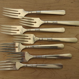 May include: Seven silver forks with ornate handles. The forks are arranged in a row, with the handles pointing to the right.