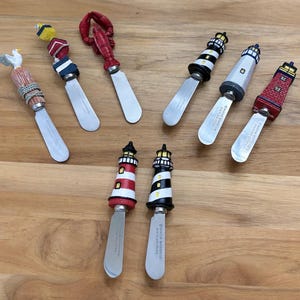 May include: Set of nine decorative butter knives with various nautical themes. The knives feature a lobster, a seagull, a lighthouse, and a nautical rope design. The handles are made of painted resin and the blades are stainless steel.
