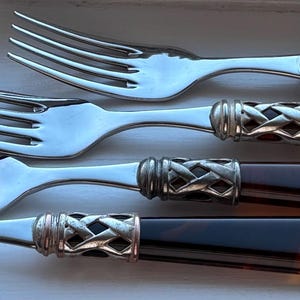 May include: Set of four stainless steel forks with dark brown, tortoiseshell-style handles. The forks have a decorative silver band where the handle meets the tines. The tines are long and slender.