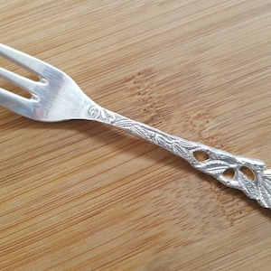 May include: A silver fork with an ornate rose design on the handle. The fork has three tines and is approximately 15 cm long.