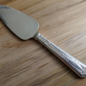 May include: A silver cake server with an ornate handle. The handle features a floral design and is slightly curved.