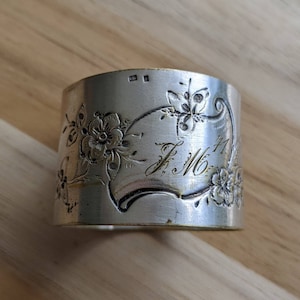 May include: Silver napkin ring with an engraved floral design and the initials "F.M." and the number "71".