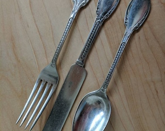 May include: A set of three silver-plated utensils, including a fork, knife, and spoon. The utensils have ornate handles with a floral design.