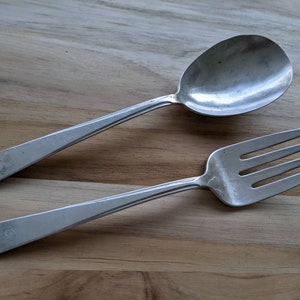 May include: A silver spoon and fork set on a wooden surface. The spoon has a rounded bowl and a long handle. The fork has four tines and a long handle.