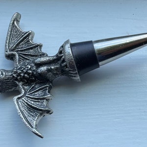 May include: Silver bat-shaped bottle stopper with a black rubber stopper. The bat has detailed wings and a textured surface.