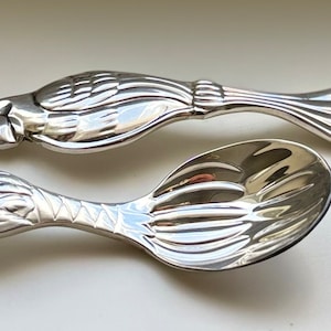 May include: A set of two silver-plated baby spoons with animal designs. One spoon features a parrot with a detailed design and the other spoon features a monkey with a detailed design.