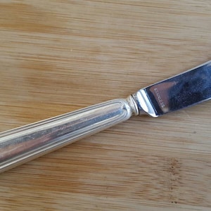 Puede incluir: Un cuchillo de mantequilla de plata con un mango redondeado y una hoja ligeramente curvada.