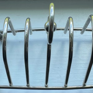 Op de afbeelding: Zilverkleurige metalen messenhouder met vijf vakken om messen in te bewaren. De messenhouder heeft een afgeronde handgreep aan de bovenkant.