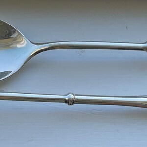 May include: A set of two silver serving utensils, one with a spoon-shaped head and the other with a slotted head.