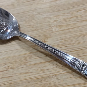 May include: A silver spoon with an ornate design on the handle and a decorative image on the bowl. The handle is inscribed with "International Silver Co. 1920."