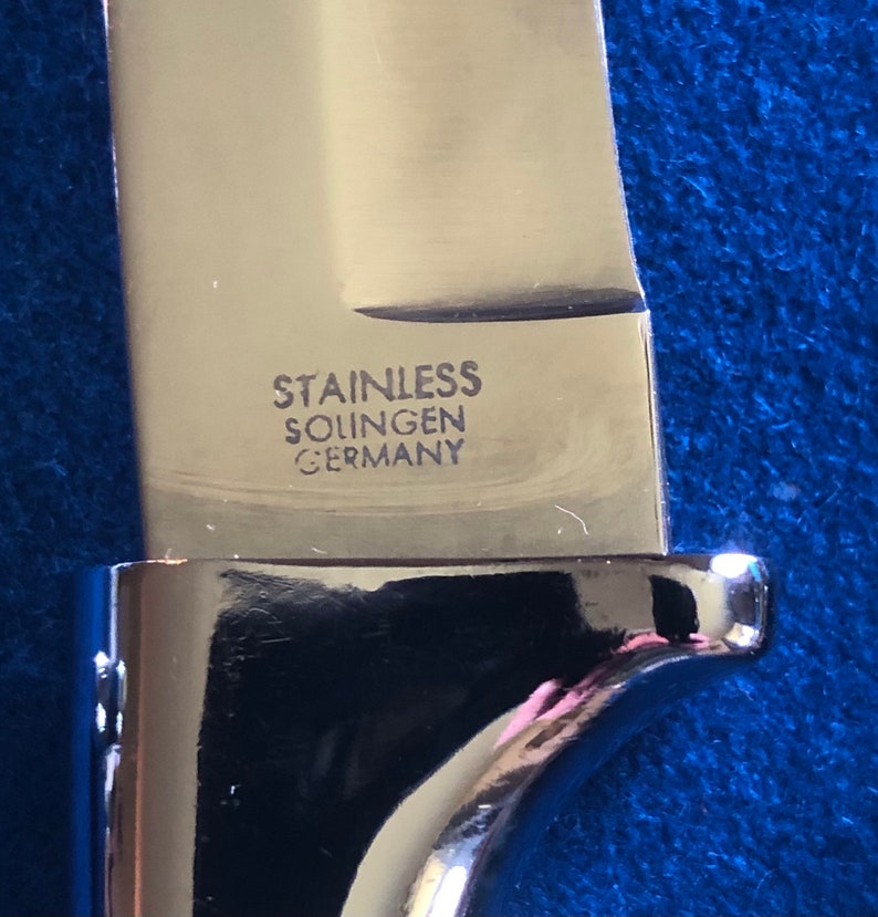 May include: Close-up of a silver knife blade with the words "Stainless Solingen Germany" engraved on the side.