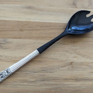May include: A black plastic salad serving spoon with a silver handle. The handle has a decorative design.