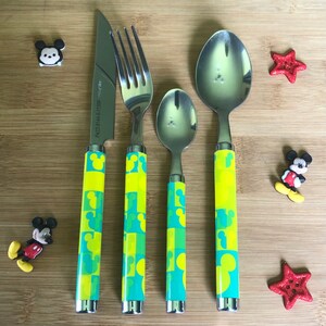 May include: A set of four yellow and blue Mickey Mouse themed cutlery pieces, including a knife, fork, teaspoon, and tablespoon. The handles are decorated with a repeating pattern of Mickey Mouse heads.