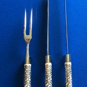 May include: Three silver kitchen utensils with black and white patterned handles. The utensils include a carving knife, a meat fork, and a carving skewer.