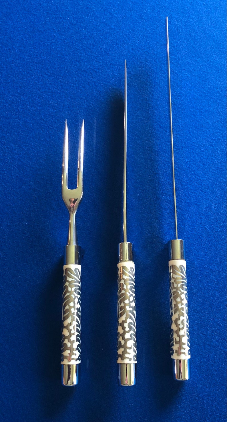 May include: Three silver kitchen utensils with black and white patterned handles. The utensils include a carving knife, a meat fork, and a carving skewer.