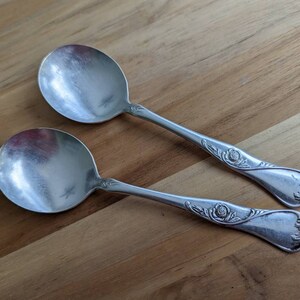 Puede incluir: Dos cucharas de plata con diseños florales ornamentados en los mangos. Las cucharas tienen una forma de cuenco redondeada y un acabado pulido.