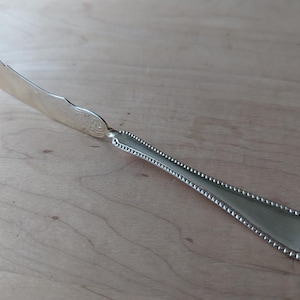 May include: A silver butter knife with a beaded handle and a slightly chipped blade.