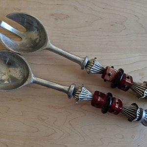 Puede incluir: Un juego de dos utensilios para servir ensalada de plata con mangos decorativos. Los mangos están adornados con cuentas de vidrio rojas y negras.