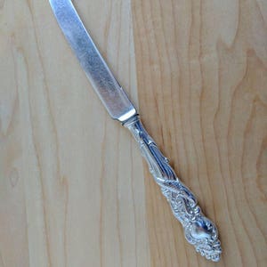 May include: A silver butter knife with an ornate handle. The handle has a floral design.