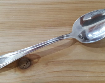 May include: A silver spoon with a floral design on the handle. The spoon is on a wooden surface.