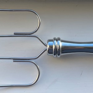 May include: A silver grilling fork with three prongs and a long, curved handle.