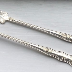 May include: Two silver forks with ornate handles. The forks have a decorative pattern of grapes and leaves.