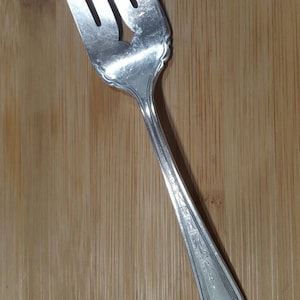 Könnte beinhalten: Eine silberne Gabel mit einem verzierten Griff. Die Gabel hat vier Zinken und ist in gutem Zustand.