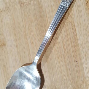May include: A silver spoon with an ornate, floral design on the handle. The spoon has a rounded bowl and a polished finish.