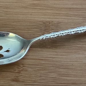 May include: A silver serving spoon with an ornate handle and a decorative cutout design in the bowl.