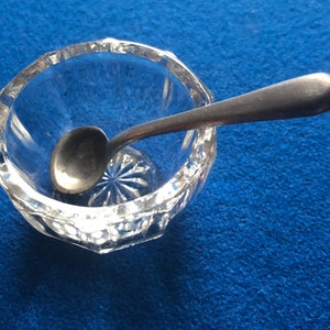 May include: A clear glass salt cellar with a cut glass design and a small silver spoon inside.