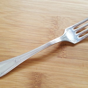 May include: A silver fork with a decorative handle. The fork is on a wooden surface.
