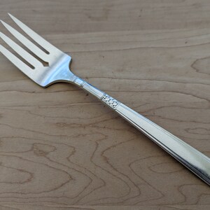 May include: A silver fork with a decorative pattern on the handle. The fork has four tines and a pointed tip.