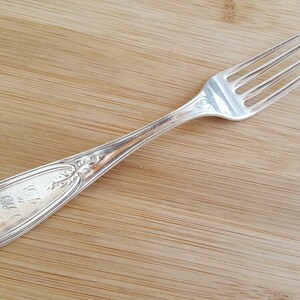 May include: A silver fork with an ornate handle and a decorative design. The fork is on a wooden surface.