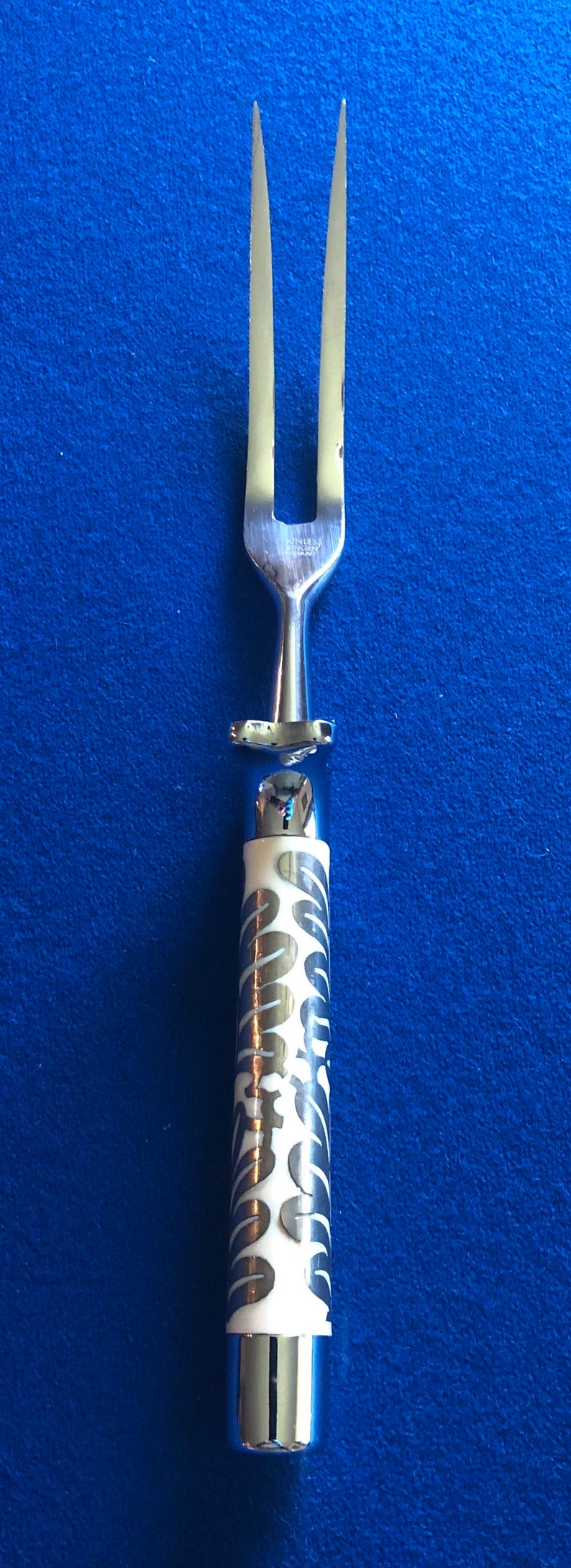 May include: A silver serving fork with a white handle featuring a silver swirl pattern. The fork has two prongs.